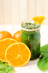 Healthy green smoothie with spinach, kiwi and orange in a retro jar on light wooden table.