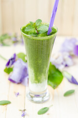 Healthy green smoothie with spinach, kiwi and orange in a retro jar on light wooden table. Flowers in the background.