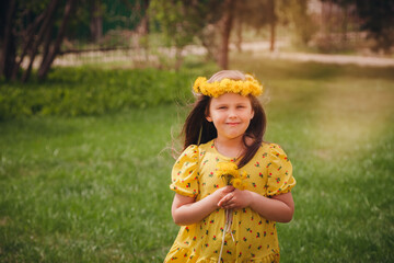 portrait of a happy girl in a yellow sundress and hair flowing in the wind with a wreath of yellow dandelions in nature, on a sunny day. 