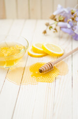 Honey dipper in honey with honeycomb, lemon, flowers and jar on light wooden table.