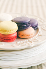 Different coloured macarons on stack of plate on white cake pedestal. Selective focus