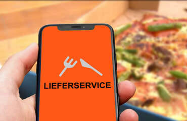 Person hält Smartphone mit einer Lieferservice App vor einer Pizza im Karton, Lieferdienst,...