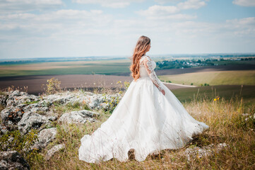 A girl in a white wedding dress stands against the backdrop of a beautiful landscape
