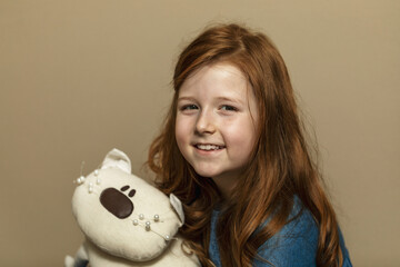 portrait of a little girl with long red hair who looks at the camera and laughs, holding a soft toy