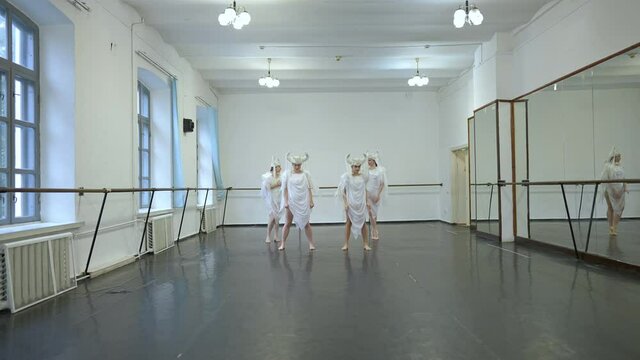 Extreme wide shot of four elegant beautiful slim Caucasian women in white angel costumes standing in dance studio preparing for rehearsal. Charming graceful young dancers training indoors