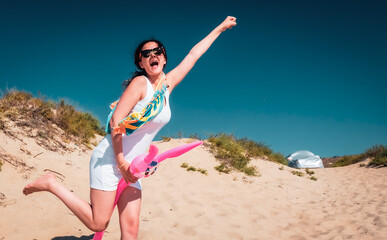 Brunette teen girl on vacation on beach. Young woman having fun playing with inflatable pink hare outdoor in the summer. Woman playing superhero