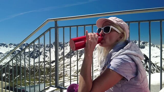 SLOW MOTION: Woman tourist drinking water bottle on the mountain peak of Aroser Weisshorn, tourist resort in Switzerland. Cable car station of Plessur Alps in Grisons Canton.