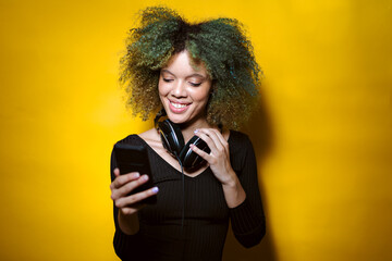 afro woman watch her phone and smiles on yellow background
