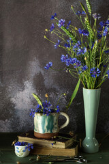 Bouquet of just cut cornflowers  with wheat plants in a vase on dark background, floral still life concept