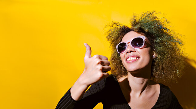 afro woman with sun grases point thumbs up on yellow background