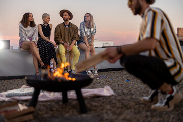 Group of young stylish friends sitting near the fireplace, hanging out together on the rooftop...