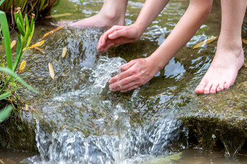 Young boy playing with clear water at a little creek using his hands and the water spring cooling his hands and refreshing with the pure elixir of life for zen meditation or environmental protection