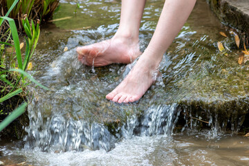 Young boy playing barefoot with clear water at a little creek using his feet and the water spring cooling his toes and legs and refreshing with the pure elixir of life in zen meditation atmosphere