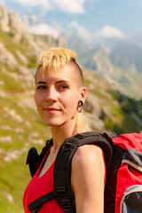 portrait of young caucasian woman smiling and doing sport with mountain in background. hiker person with backpack and happy.