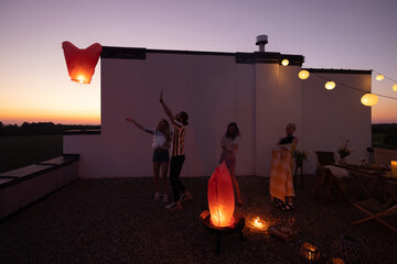 Young people launch sky lanterns during party on the rooftop terrace. Romantic and fun summertime...