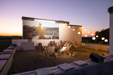 Small group of people watching movie on the rooftop terrace at sunset. Open air cinema concept....