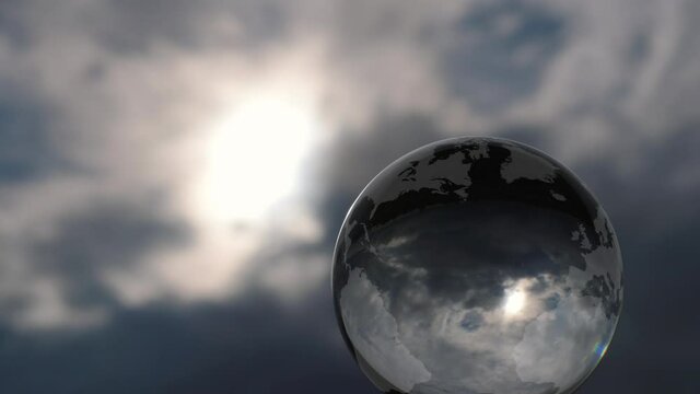 Glass Earth with a dramatic cloud background.
World map etched onto a rotating glass sphere with a turbulent sky refracted in it.