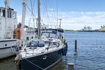 Fototapeta premium Sail yacht standing moored in the sea port, sailboat harbor Helsinki, Finland. Modern water transport, lifestyle. Three modern icebreakers in the background. Yachting, marine background.