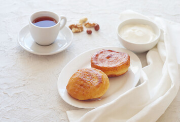 Pancakes are in a plate on the table, behind sour cream and tea. Nice breakfast.