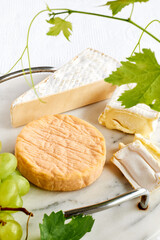 Delicious cheese brie or camembert on cutting board with bunch of grape on the table with white tablecloth. Dairy products. Italian, French cheese. Breakfast. Selective focus
