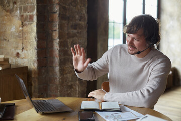 Serious young caucasian man speaking by video call and looking at laptop and writing at notepad....