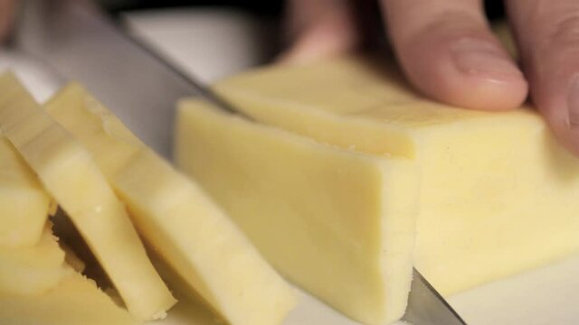 knife cutting block of cheese into slices close up