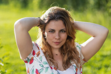 Atractive beautiful  young woman with both hands in her hair is posing outdoors. Horizontally. 