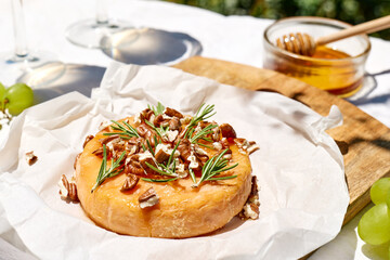 Baked brie or camembert with rosemary, nuts and honey on cutting board on the table in the garden. Dairy products. Italian, French cheese. Breakfast. Selective focus
