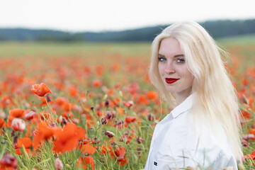 Obraz na płótnie Canvas Portrait of blonde young woman posing in red poppy field looking at the camera. Horizontally. 