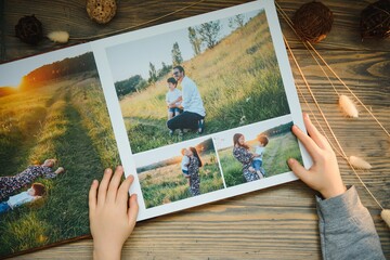 the Hand child holding a family photo album against the background of the a wooden table - obrazy, fototapety, plakaty