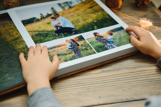the Hand child holding a family photo album against the background of the a wooden table