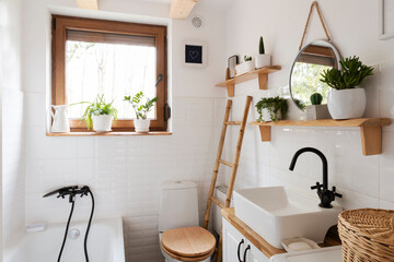 Small bathroom in a cottage in rural style with bath, toilet, stylish sink, wood, round mirror and...