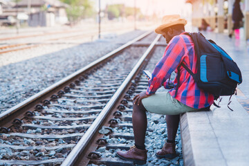 African male traveler waiting for the train on railway station with using smartphone. Adventure travel concept