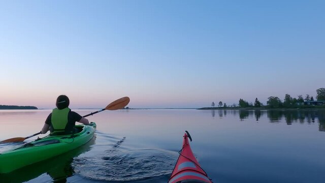 Girl kayaking and then taking break from paddling, looking at mobile phone, mirror like calm water at midnight in Northern Sweden during light Summer night Sun in polar regions. Umea, Sweden.