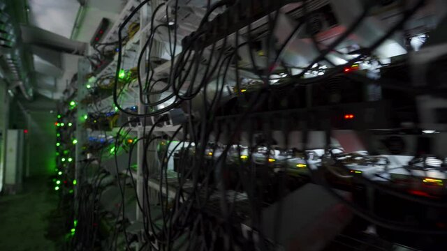 Bitcoin miners in large farm. ASIC mining equipment on stand racks mine cryptocurrency in steel container. Blockchain techology application specific integrated circuit datacenter. Server room lights.
