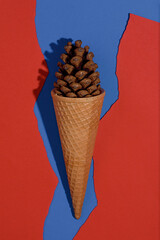 Ice cream cone decorated with a pine cone. Red and blue in the background. Summer concept. 