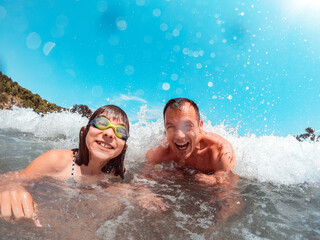 Father and daughter getting splashed by the sea wave