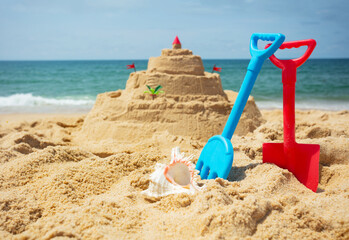 Fototapeta na wymiar Toy rake and scoop near sand castle on background