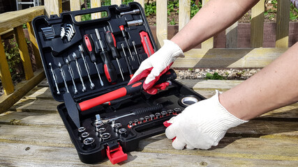 the hands of a man in work gloves open a suitcase with various tools. to work, you will need a screwdriver, keys, a tape measure
