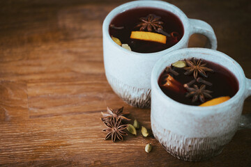 Two cups of autumn mulled wine or gluhwein with spices and orange slices on rustic table copyspace. Traditional drink on autumn holiday on the background of autumn leaves