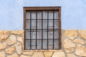 Fototapeta na wymiar Rustic window with forged grating in a stone facade.