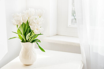 Bouquet of white tulips in white ceramic jug on table. Spring concept