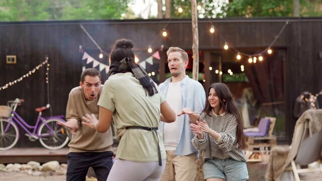 Multiethnic adult friends having fun playing blind man's buff tag game at summer party. Blindfolded young woman attempting to touch other players grimacing around her in backyard