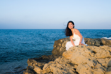 young Asian woman by blue sea -  happy and beautiful Chinese girl  enjoying holiday trip relaxed and cheerful at beach rock cliff during summer in tourist  travel concept