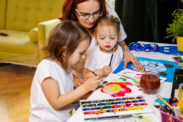 Family hobbies leisure activity home concept. Mother and small daughter drawing with fun using paintbrushes and watercolors. Children and parent creating picture together, body paint, home quarantine