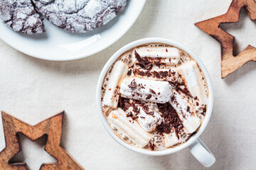 Christmas or New Year festive background. Hot chocolate or cocoa with marshmallows in white cup, christmas decorations, top view, white fabric background.
