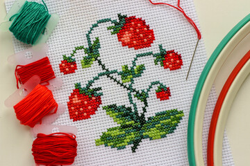 Red ripe strawberries embroidered with a cross-stich on a white canvas by hand. With a needle, thread floss and hoop.