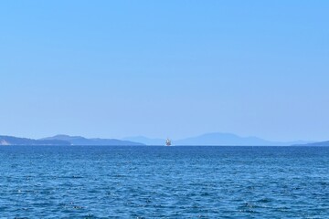 Obraz premium Seascape. Approaching ship in the distance on horizon of sea, mountains and sky