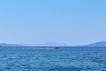 Seascape. Motor boat in the distance on horizon of sea, mountains and sky