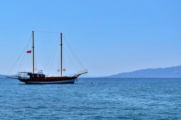Fototapeta na wymiar Seascape. Two-masted sailboat in sea bay on sunny day against background of mountains and blue sky